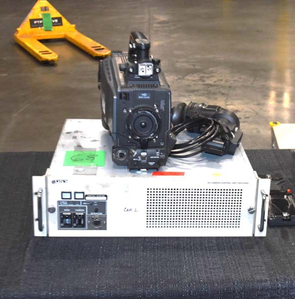 Professional video camera on a control unit with coiled cables on a black surface.