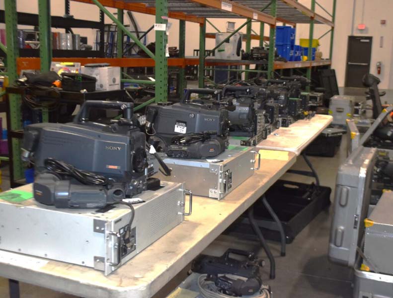 Row of Sony video cameras on metal cases in a storage area.